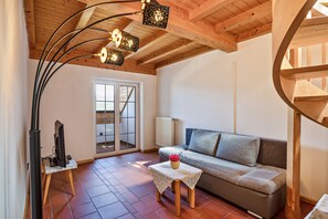 A cozy living room with a sofa, a table with a vase, a television on a stand, and a spiral staircase.