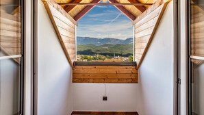 Una habitación con techo inclinado, vigas de madera y vistas a montañas a través de una ventana.