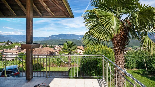 Un balcón con vistas a un pueblo, una palmera y montañas al fondo.