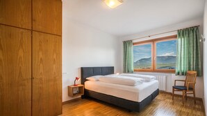 Une chambre à coucher comprenant un lit, une table de chevet, une chaise, une armoire et une fenêtre donnant sur un beau paysage.