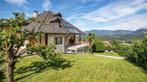 Une maison avec un toit en pente, des panneaux solaires, un balcon et une vue sur les montagnes.