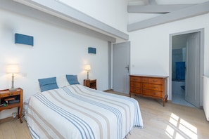 Un dormitorio con cama, mesitas de noche, cómoda y un baño visible a través de una puerta abierta.