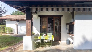 Une terrasse avec une table et des chaises, un barbecue et un chemin de pierre menant à une maison avec un toit en tuiles.