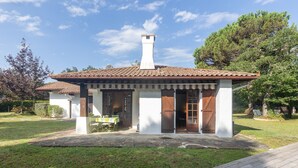 Une maison avec un toit en tuiles, une cheminée et une véranda à l’avant, avec une table et des chaises.