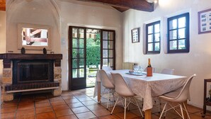 Un coin repas avec une cheminée, une table dressée pour deux personnes et une vue à travers la porte vitrée.