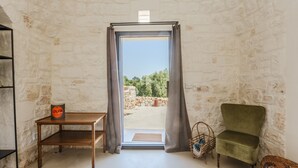A room with a stone wall, a wooden table, a green chair, and a view through a doorway. - Villa 'Trulli Meridiem Con Piscina' with Private Pool, Wi-Fi and Air Conditioning (Ostuni)