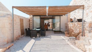 A covered outdoor seating area with wicker chairs, a table, and a stone wall backdrop. - Villa 'Trulli Meridiem Con Piscina' with Private Pool, Wi-Fi and Air Conditioning (Ostuni)