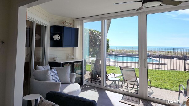A modern living room with a large sliding glass door leading to a balcony with a pool view. - Whitney Beach 321 2brm beachfront (Longboat Key)