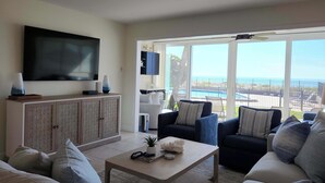 A living room with a large TV, a wooden cabinet, and a sofa set. - Whitney Beach 321 2brm beachfront (Longboat Key)