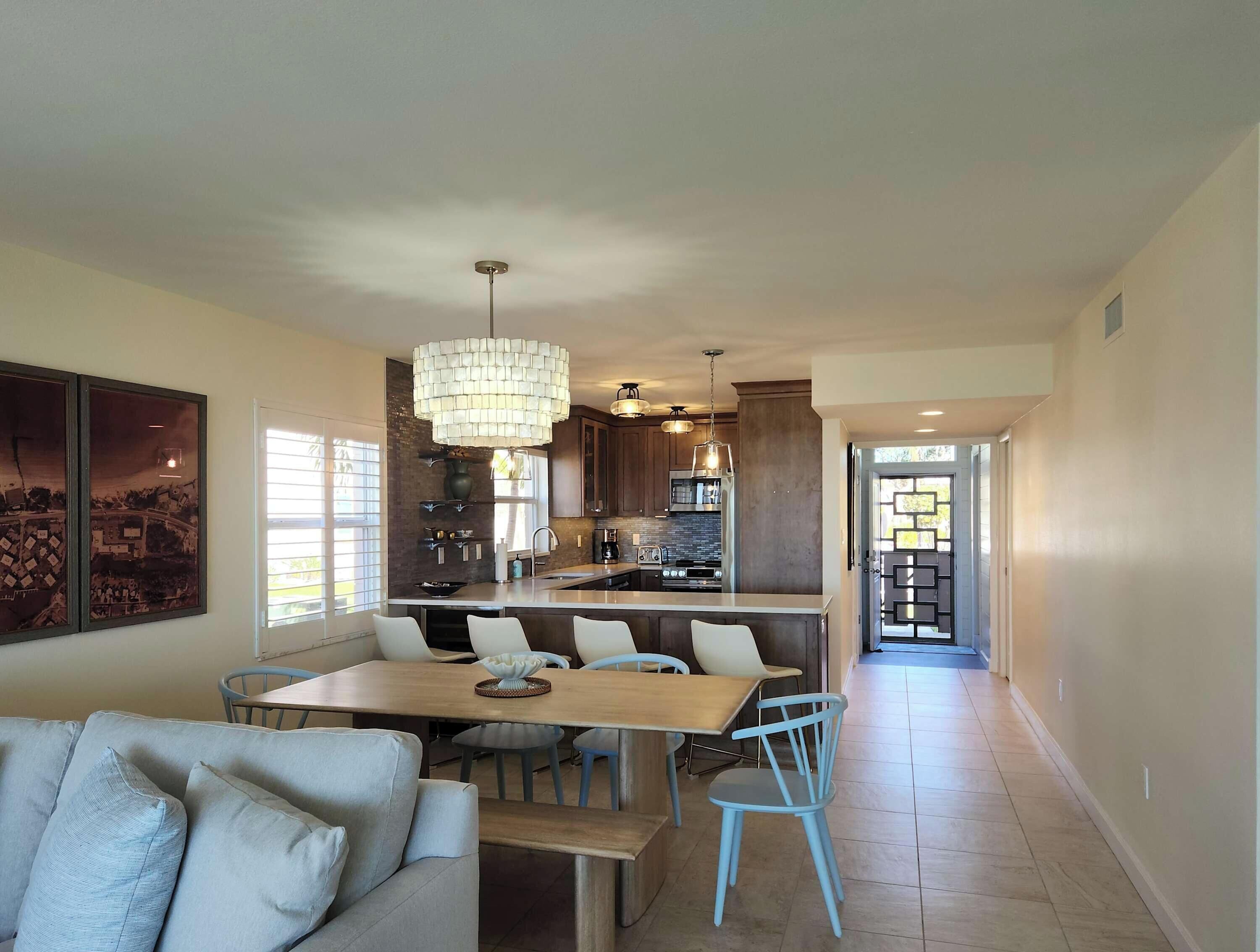 A modern kitchen with a central island, pendant lighting, and a dining area with a wooden table and blue chairs.