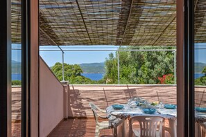 Eine Terrasse mit Esstisch, mit Blick auf eine malerische Landschaft mit Bäumen und einem Gewässer.