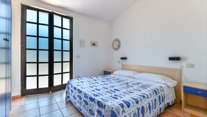Un dormitorio con una cama, una mesita de noche, un reloj de pared, un enchufe y una puerta con paneles de vidrio esmerilado.
