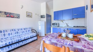 A compact living space with a sofa, a dining table set for two, and a kitchenette with blue cabinets and white appliances.