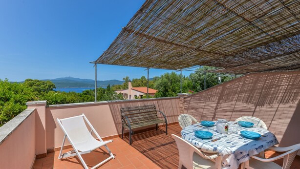 A terrace with a table set for dining, a chair, and a sun lounger.
