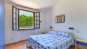 A bedroom with a bed, a window, a mirror, and a small bedside table.