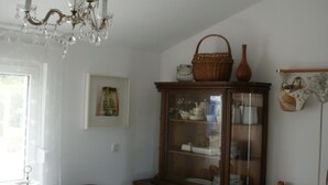 Un comedor con una mesa blanca, sillas, una araña y un aparador de madera con puertas de cristal.