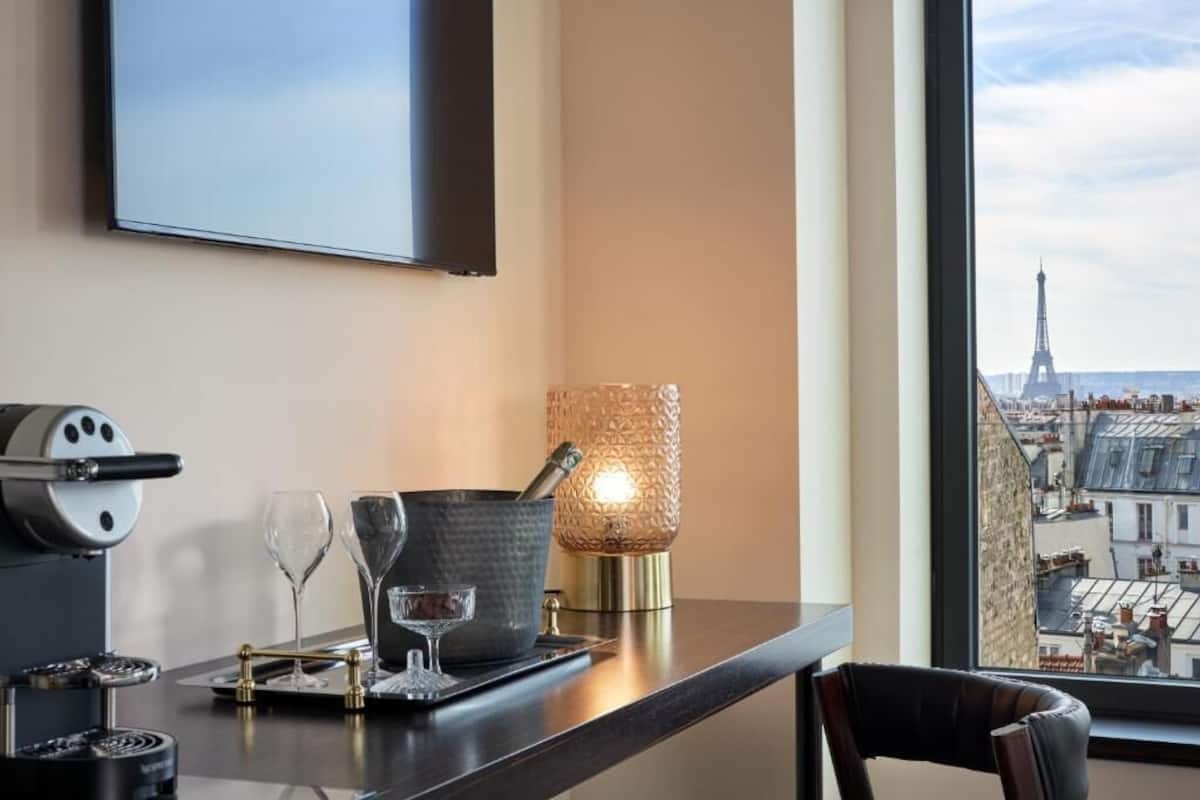 Habitación de hotel con vista a la Torre Eiffel, una cafetera, un vaso de agua y una lámpara decorativa.