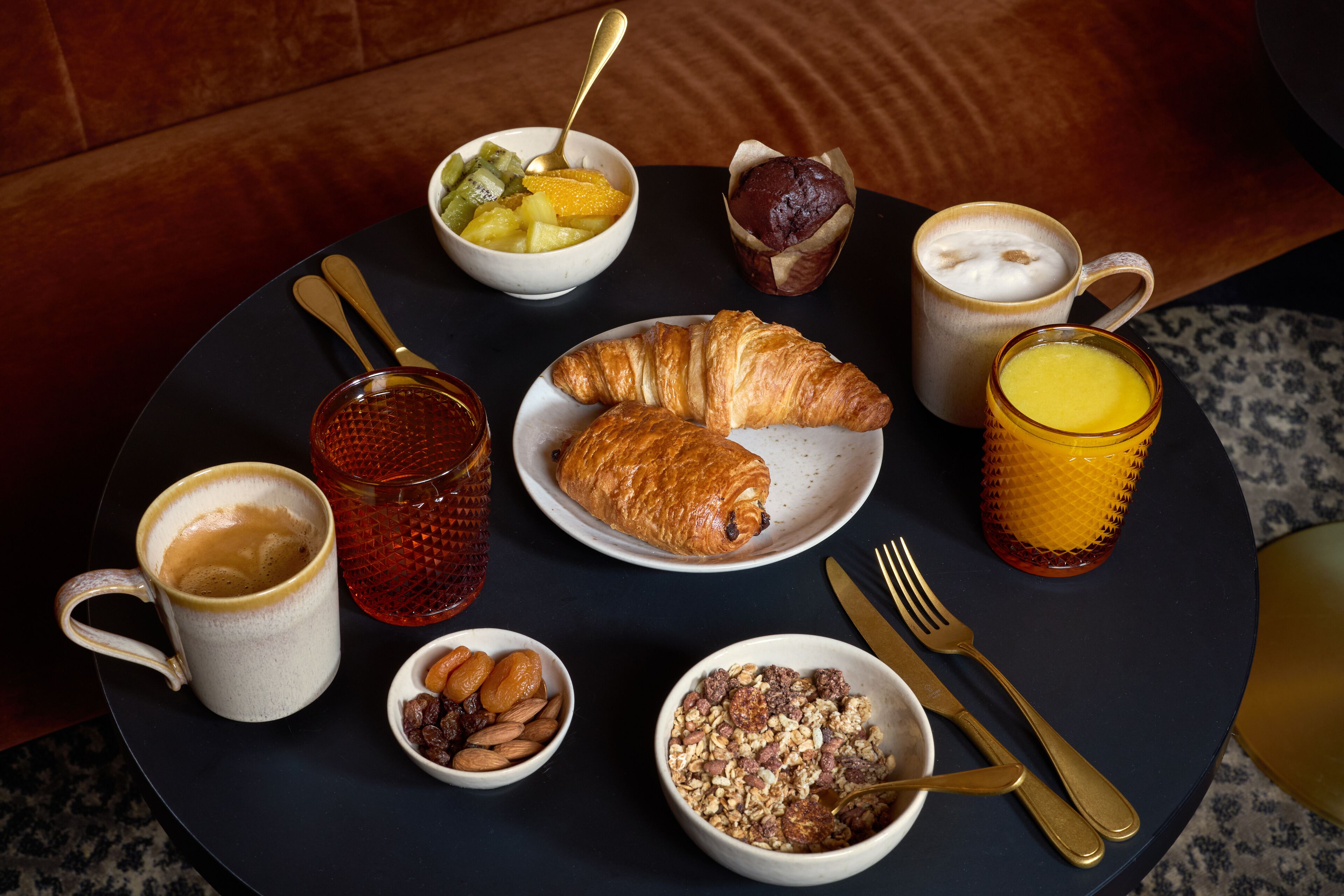 Une table ronde dressée pour le petit-déjeuner, avec des croissants, des fruits, du café et du jus.