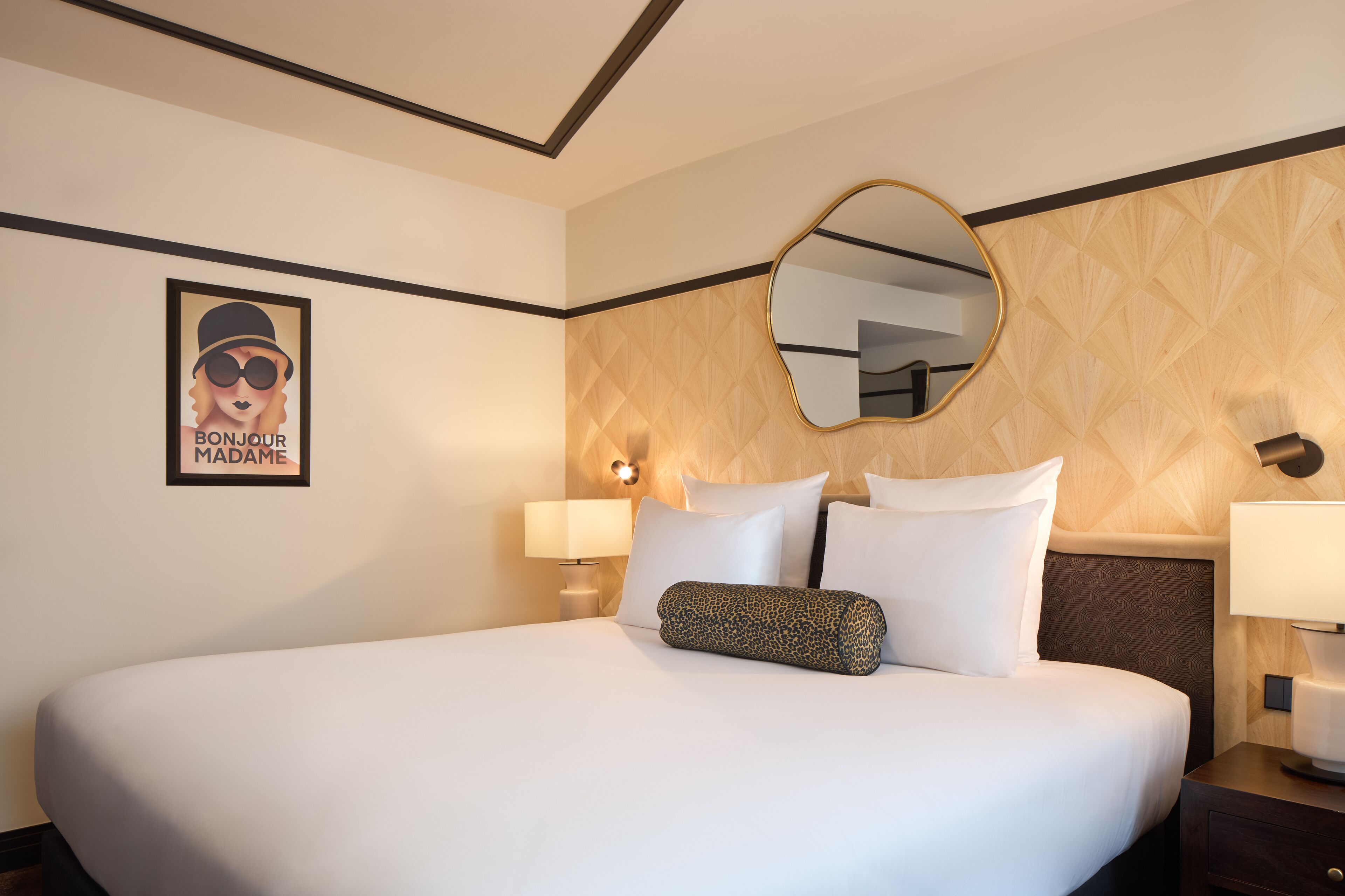A hotel room with a large bed, two bedside lamps, a wall-mounted mirror, and a poster on the wall.