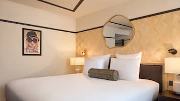 A hotel room with a large bed, two bedside lamps, a wall-mounted mirror, and a poster on the wall.