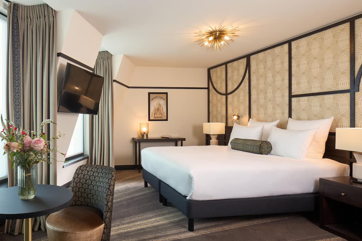 Habitación de hotel con una cama grande, televisión montada en la pared, escritorio con lámpara y una silla.