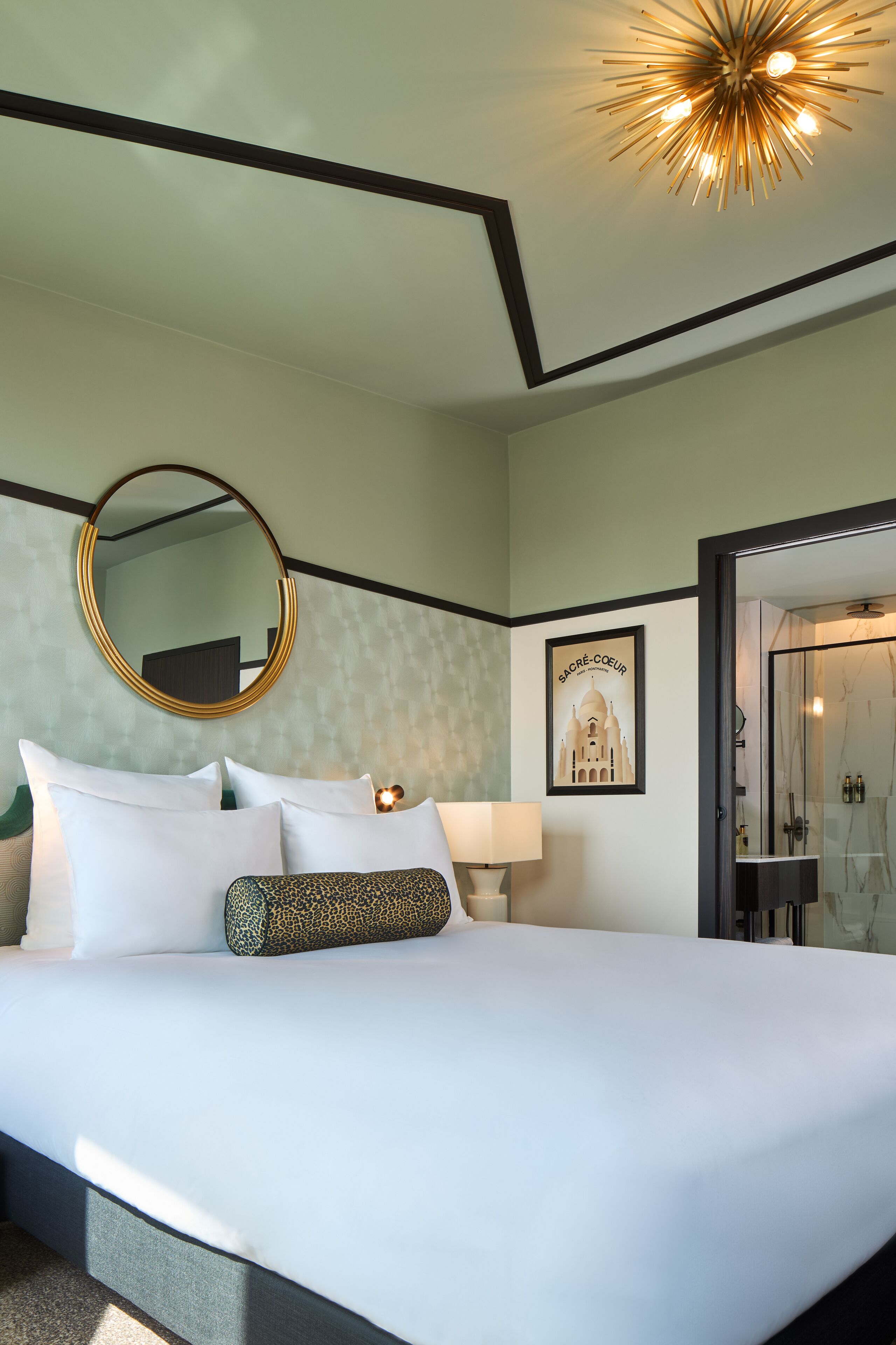 Habitación de hotel con una cama grande, un espejo redondo, un cuadro enmarcado y una zona de ducha.