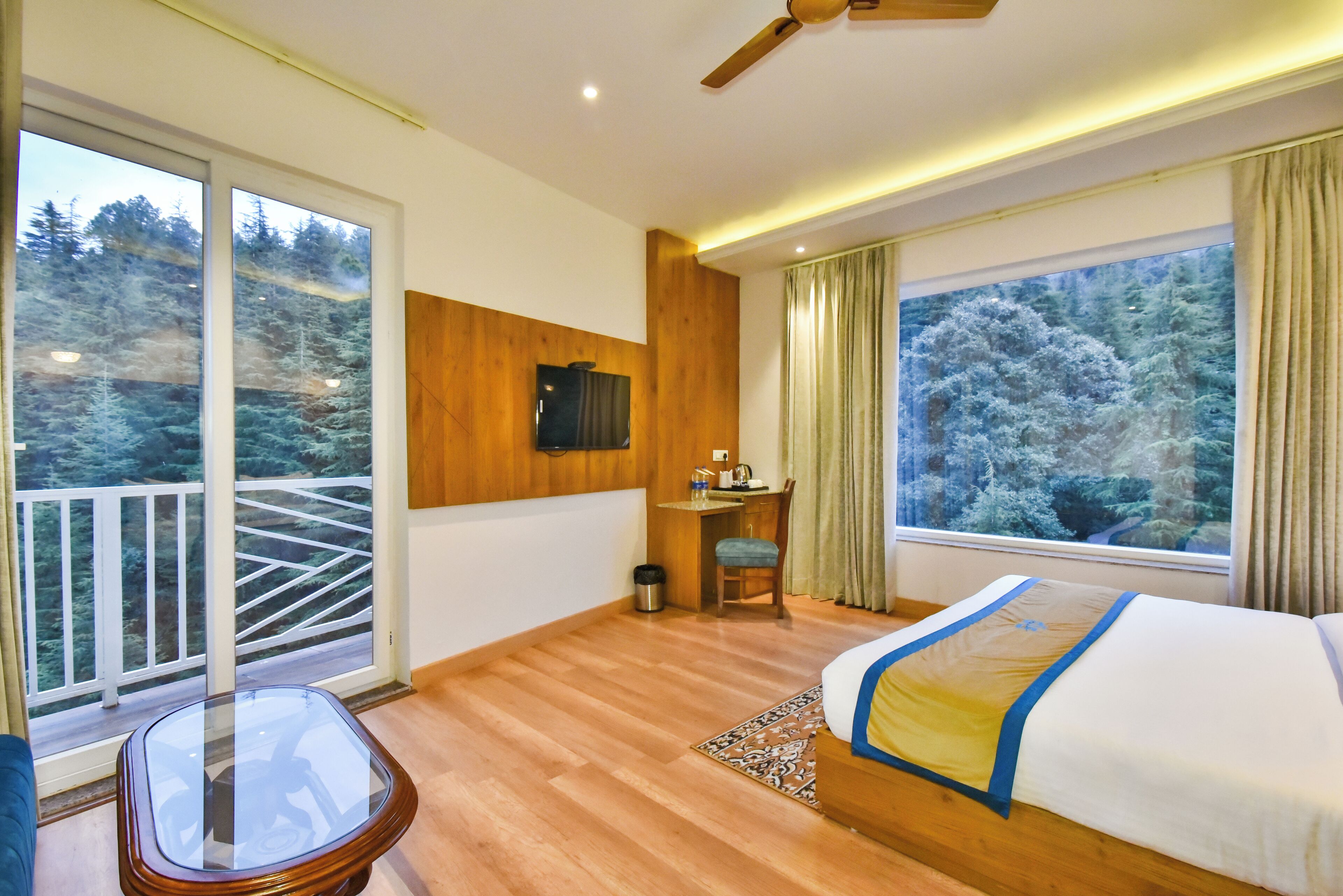 A hotel room with a balcony, a bed, a desk, and a TV.