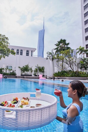 A poolside setting with a dining table and drinks, surrounded by palm trees and a modern building in the background. - Hotel Royal Signature (Kuala Lumpur)