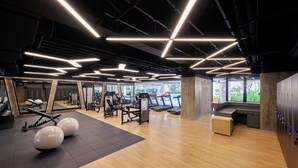 Ein modernes Fitnessstudio mit Trainingsgeräten, Holzböden und einem großen Fenster, das natürliches Licht hereinlässt.