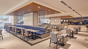Eine moderne Hotelhalle mit einer Sitzecke, Esstischen und einer Küche im Hintergrund.