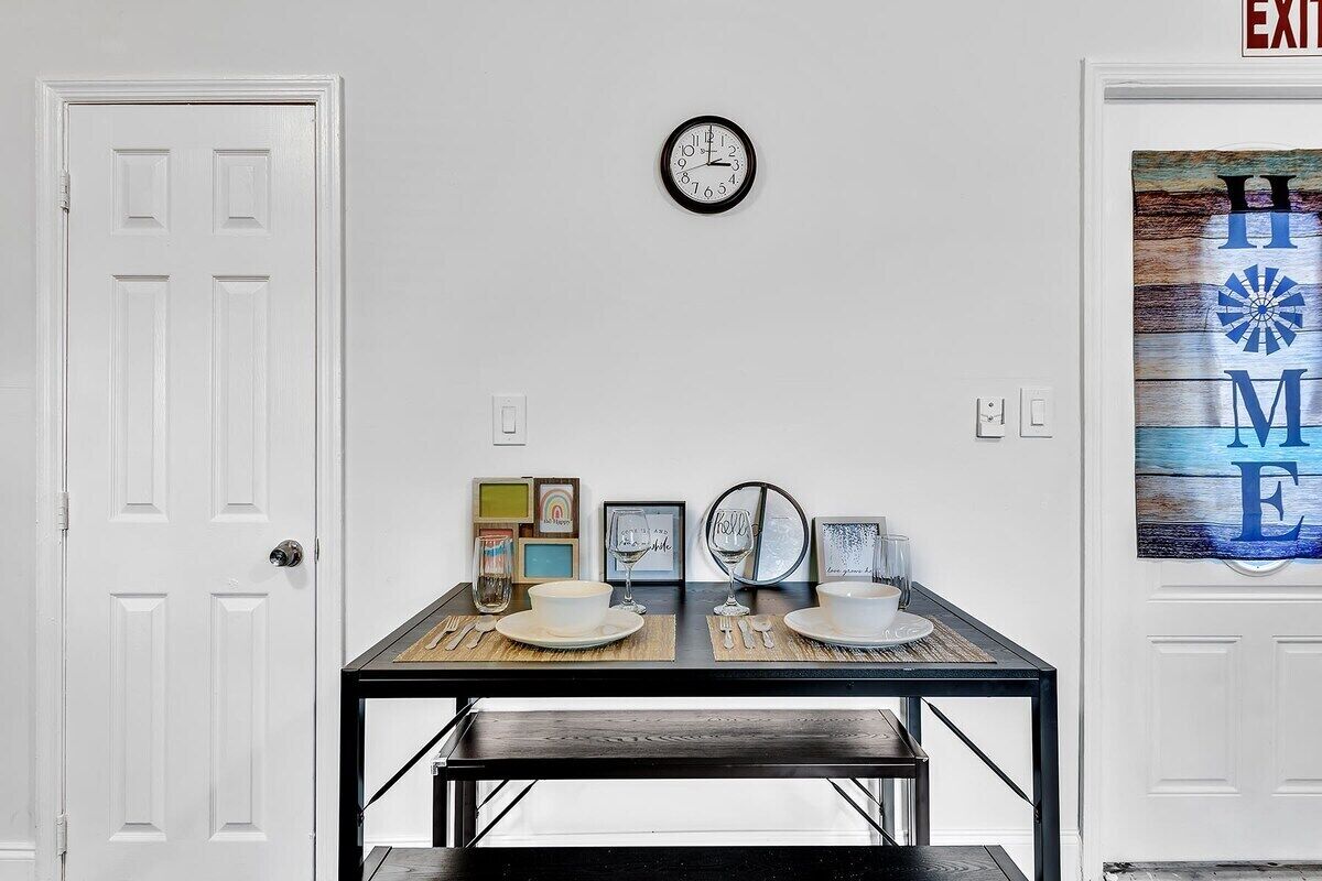 A dining area with a table set for two, a wall clock, and framed pictures.
