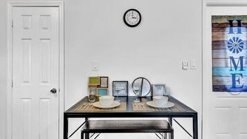 A dining area with a table set for two, a wall clock, and framed pictures.