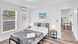 A modern bedroom with a bed, bedside tables, a window with blinds, and a painting on the wall. - Hallandale Mins From Beach & Aventura Mall HN01 (Hallandale Beach)