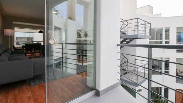 A modern apartment with a glass door leading to a balcony, a staircase, and a view of the cityscape.