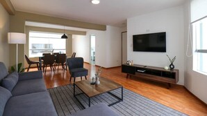 A modern living room with a sofa, coffee table, TV, and dining area.