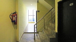 A hallway with a fire extinguisher mounted on the wall, a staircase with a metal railing, and a door labeled "205". - Hotel Raaso inn Nawada Metro By Arrow  (New Delhi)