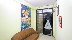 A room with a brown sofa, a colorful mural, and a black and white framed picture on the wall. - Hotel Raaso inn Nawada Metro By Arrow  (New Delhi)