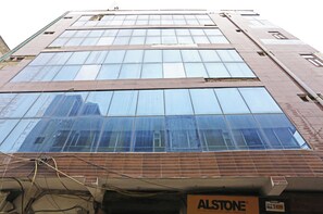 A multi-story building with large windows and a sign for 'ALSTONE'. - Hotel Raaso inn Nawada Metro By Arrow  (New Delhi)