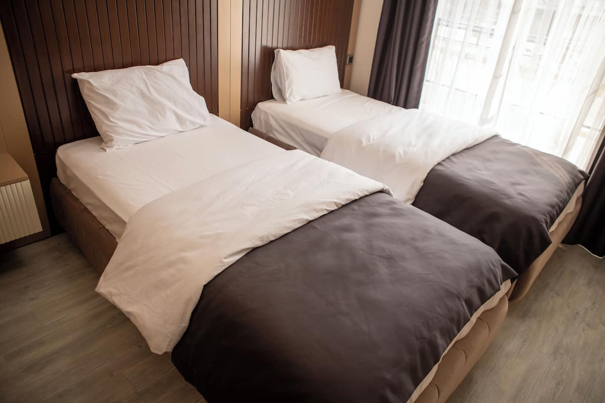 A hotel room with two beds, wooden headboards, and a window with curtains.