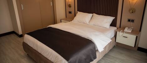 Una habitación de hotel moderna con una cama grande, cabecera de madera, dos mesitas de noche con lámparas y un armario empotrado.