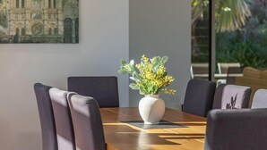 Ein moderner Essbereich mit einem Holztisch, grau gepolsterten Stühlen, einer weißen Vase mit gelben Blumen und einer Pendelleuchte.