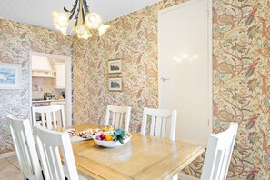 A dining area with a wooden table, white chairs, and a fruit bowl.