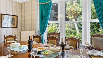 A dining room with a large table set for a meal, surrounded by ornate chairs, and large windows with curtains.