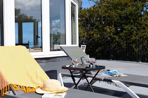 A sunlit outdoor seating area with lounge chairs, a table with drinks, and a magazine.