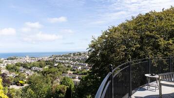 A balcony with a table and chair, overlooking a coastal town and the sea.