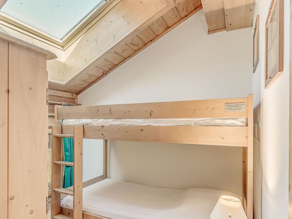 Habitación con literas, tragaluces, vigas de madera y una mesita de noche con lámpara.
