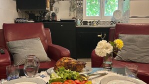 A dining table set with plates, cutlery, and a variety of dishes including a roasted chicken, salad, and corn. There are two red leather chairs and a small vase with flowers. The room has a black and white patterned backsplash and a window with a view of greenery. - La Teranga du Saulchoix (Clairy-Saulchoix)