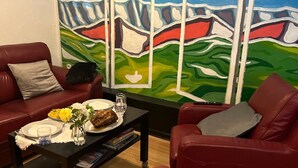 A living room with red leather sofas, a coffee table with a vase of flowers, and a painting of a landscape on the wall. - La Teranga du Saulchoix (Clairy-Saulchoix)
