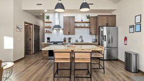 Una cucina moderna con isola centrale, illuminazione a sospensione, mobili in legno, elettrodomestici in acciaio inossidabile e un estintore a parete.