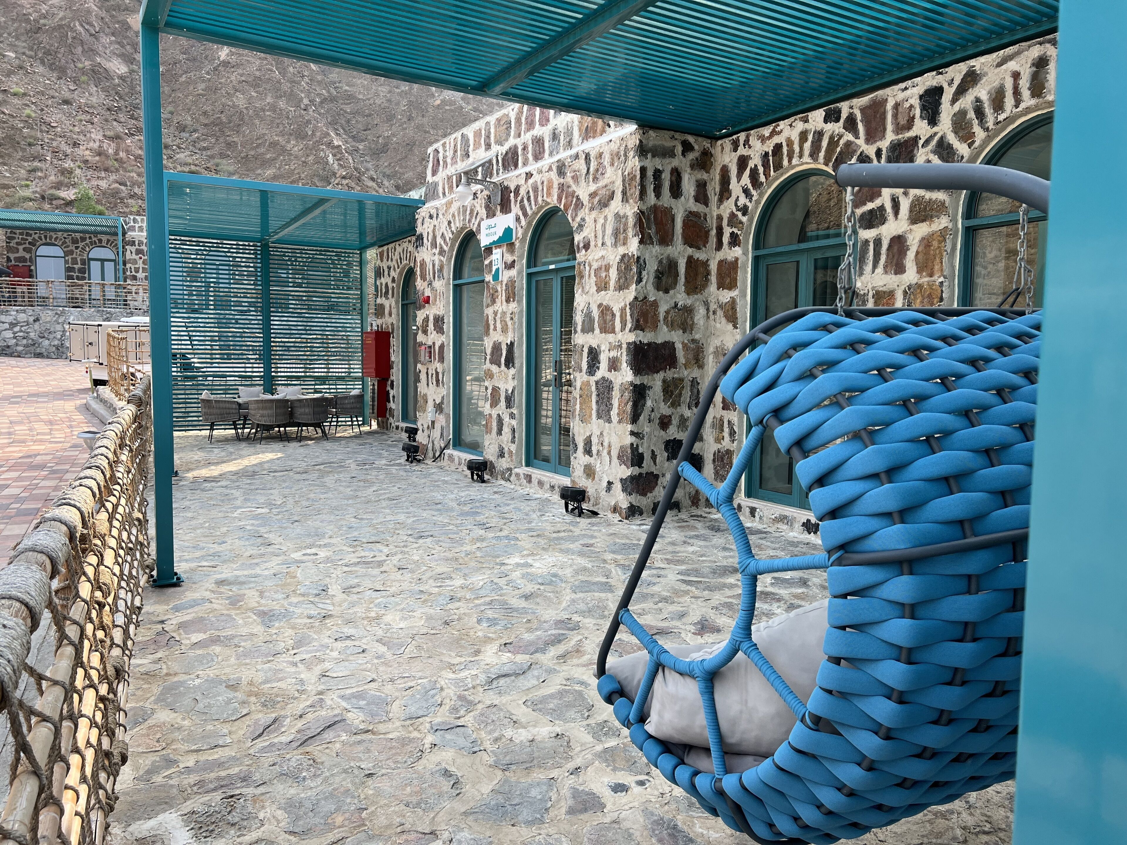 A stone building with a covered outdoor seating area, a hanging chair, and a stone floor.